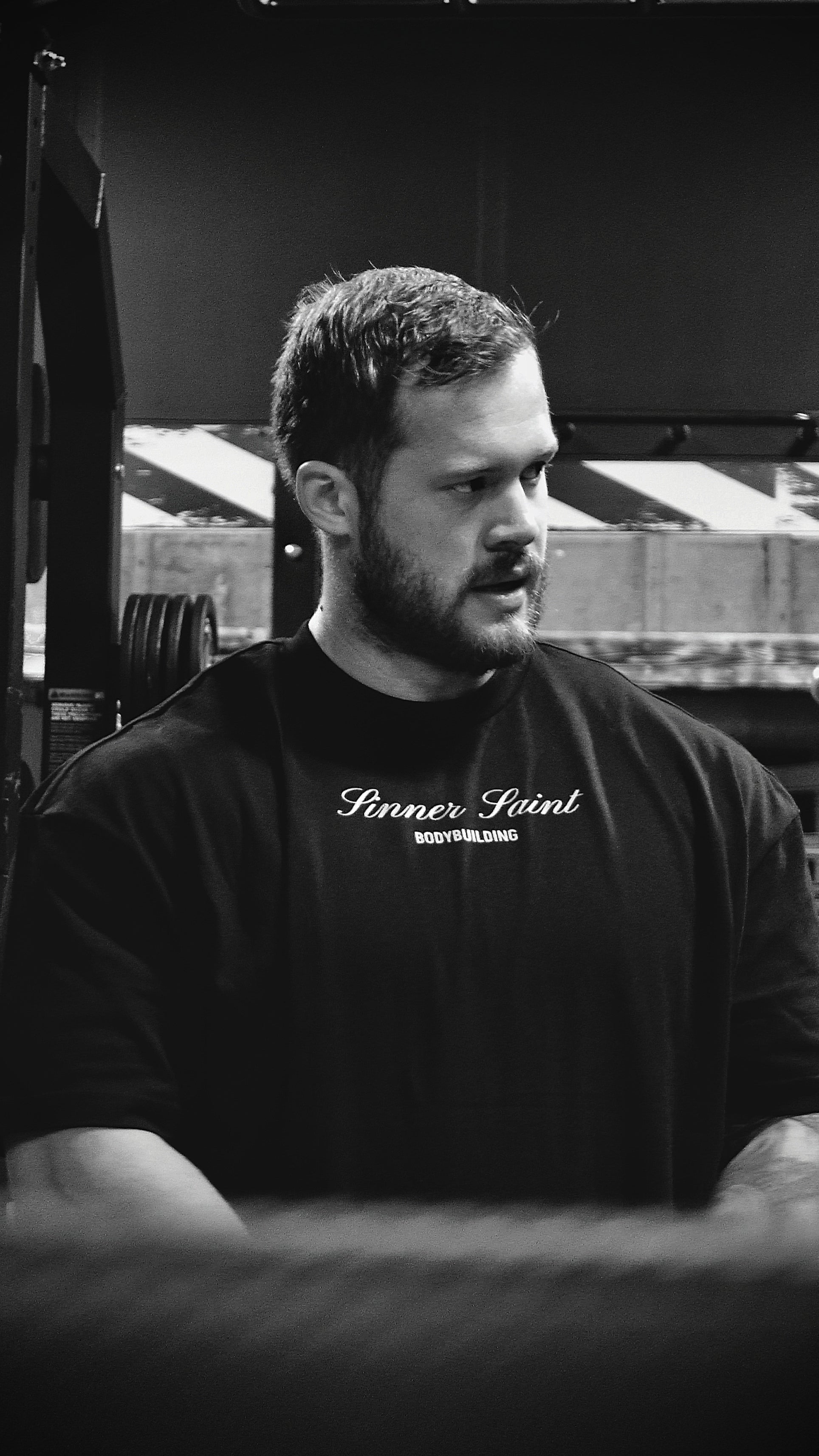 en svartvit bild på en man som bär en oversized sinner saint t-shirt som det står "sinner saint bodybuilding på"