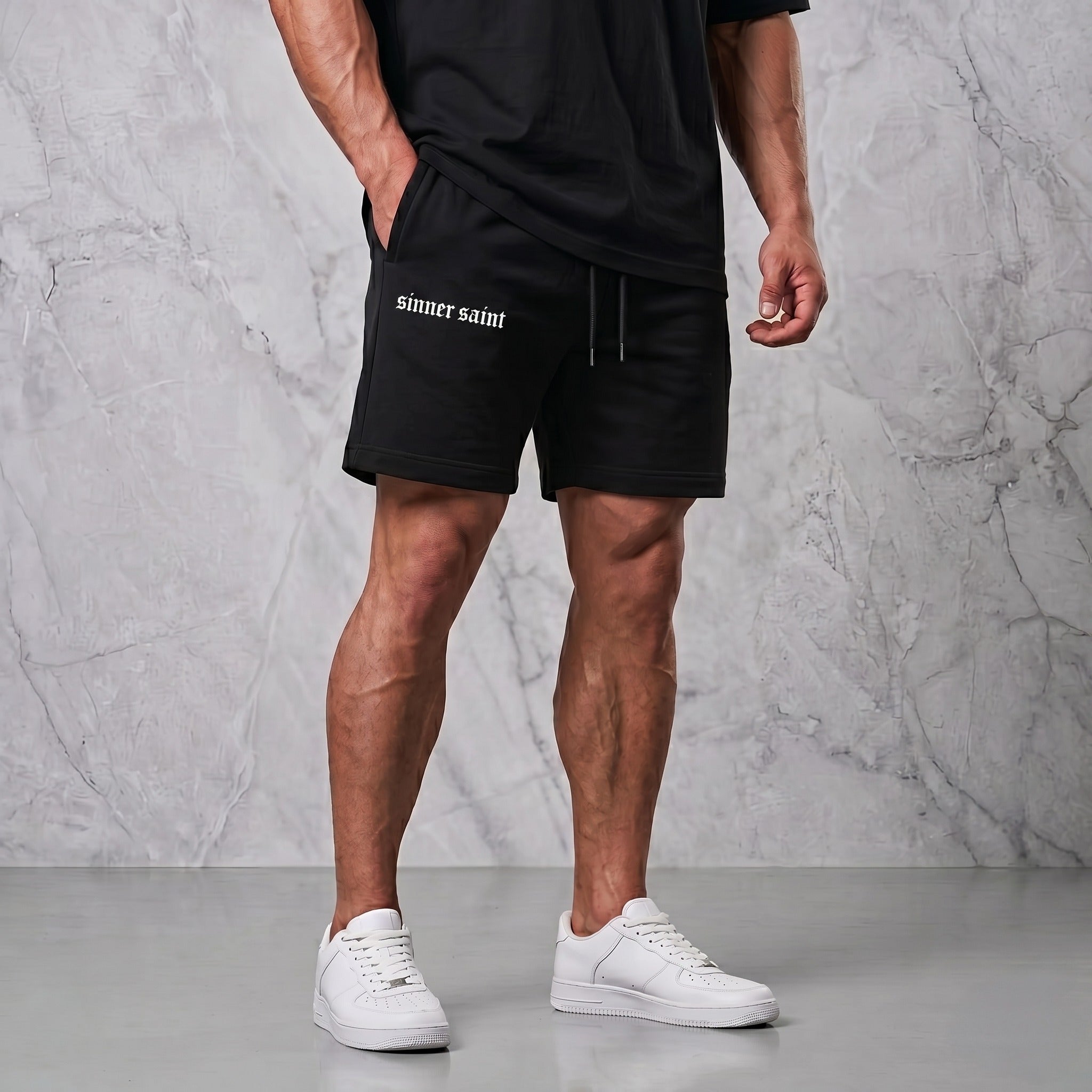 En man i en lyxig fotostudio som bär ett par svarta gymshorts där det står "sinner saint" på ena benet.